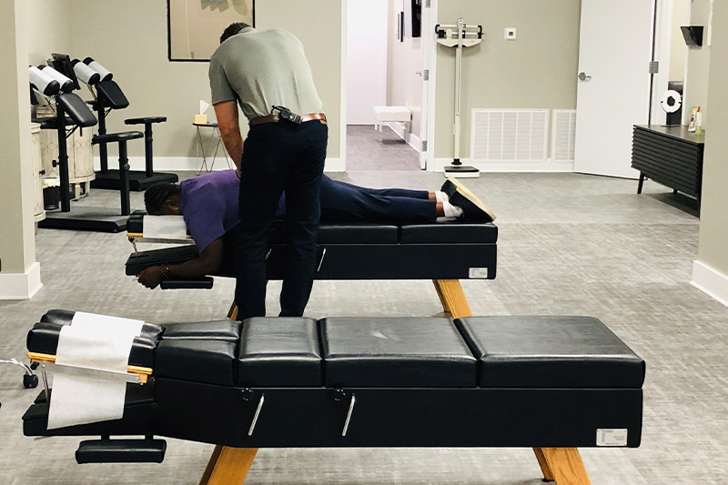 Chiropractor doing an adjustment in a treatment room with other chiropractic tables.
