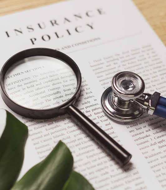 Insurance policy document laying on a desk with a magnifying glass and stethoscope sitting on top.