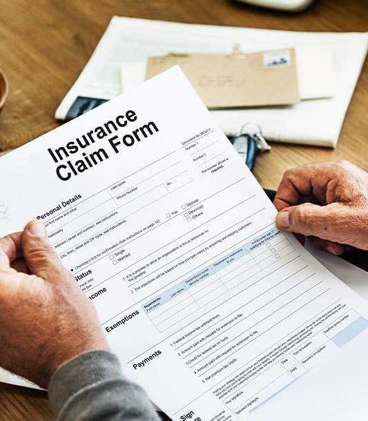 Insurance claim form being held by a man's hand over a desk.